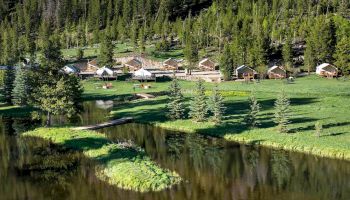 A lakeside village with wooden cabins clustered along the shore, trees lining the background, and a calm reflective water body.