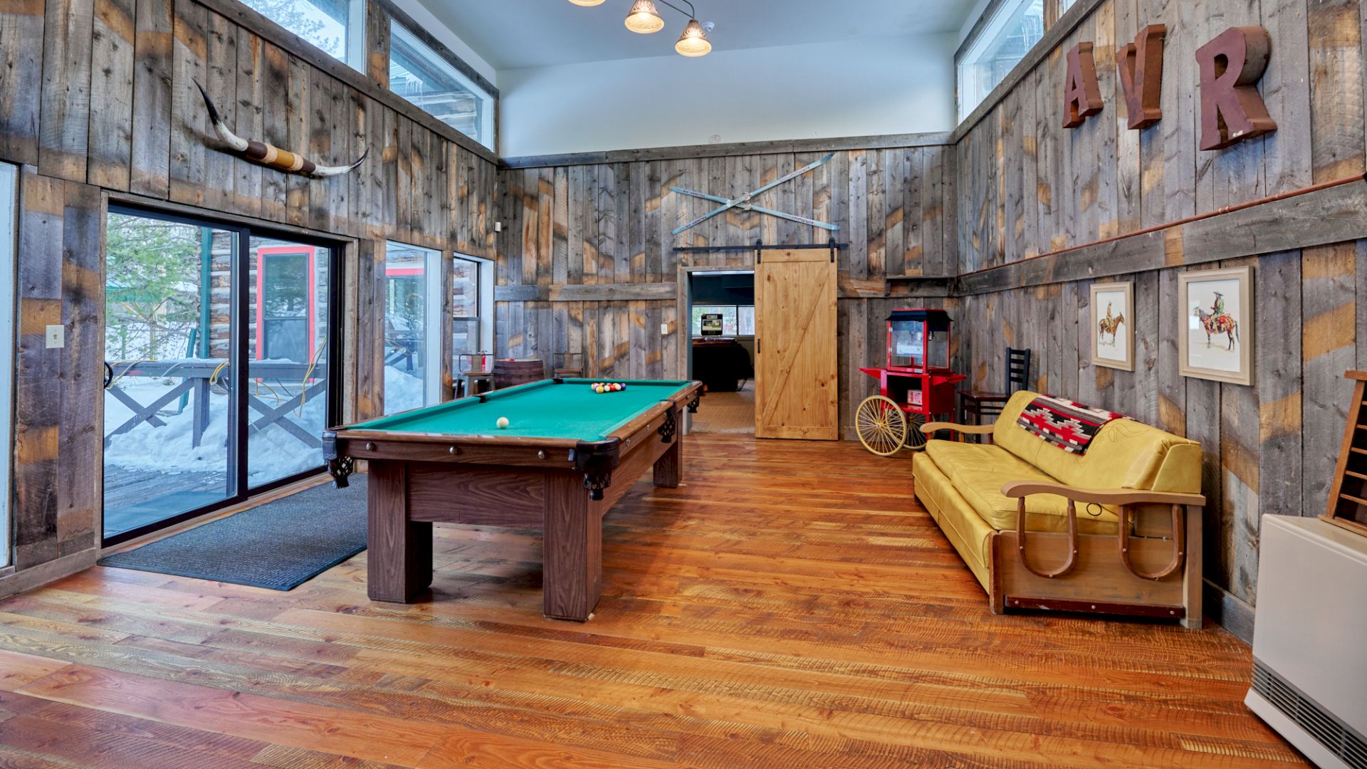 Cozy rustic game room with a pool table, wooden plank walls, a yellow couch, vintage decor, and large windows letting in natural light.