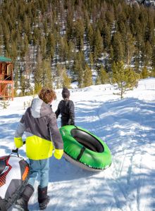 A person riding a snowmobile down a snowy, forested slope, wearing a bright yellow jacket and helmet, kicked up powder behind them.