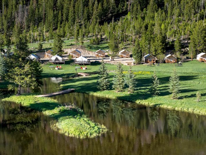 A tranquil lakeside village with wooden cabins lining the shore, evergreen trees in the background, and a calm reflective water body nearby.
