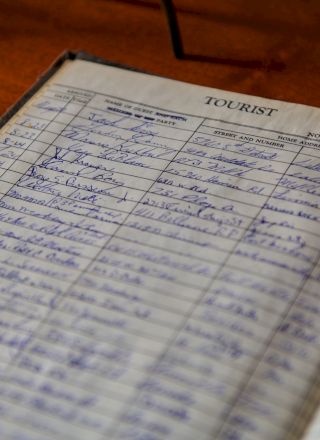 A vintage guest book or logbook open to a dated page, filled with handwritten entries and blue ink, labeled &ldquo;TOURIST&rdquo; at the top, blank spaces and lines throughout.