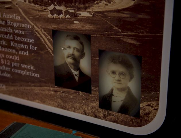 Two vintage portraits mounted on a brown display panel, with faint text beside them; the scene has a rounded white edge and a dark, warm tone.