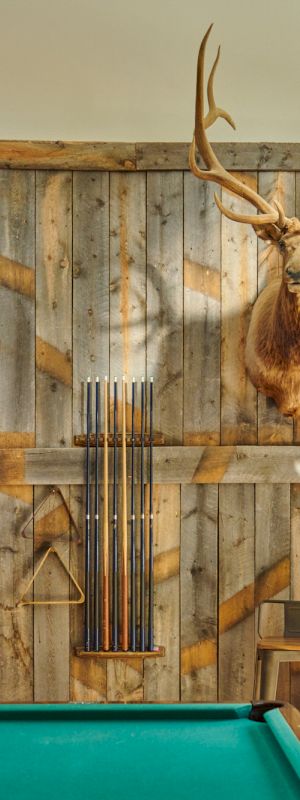 A vintage game room with a green pool table, ornate wallpaper, warm lighting, and rustic decor.