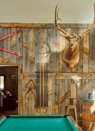A vintage game room with a green pool table, ornate wallpaper, warm lighting, and rustic decor.