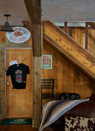 A rustic tavern scene with wooden walls, a staircase, barrels, and a man in a hat seated at a table, creating a cozy, old-time vibe.