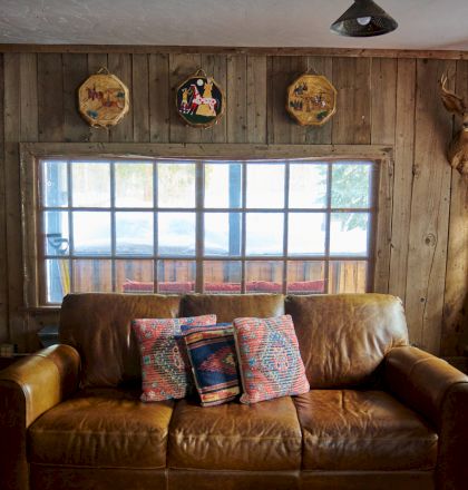 A cozy living room with warm wood tones, a plaid sofa and chairs, a coffee table, soft lighting, and large windows letting in natural light.