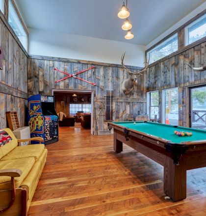 A cozy game room with a pool table, warm lighting, a kitchen, and comfortable seating in the background, perfect for socializing and play.