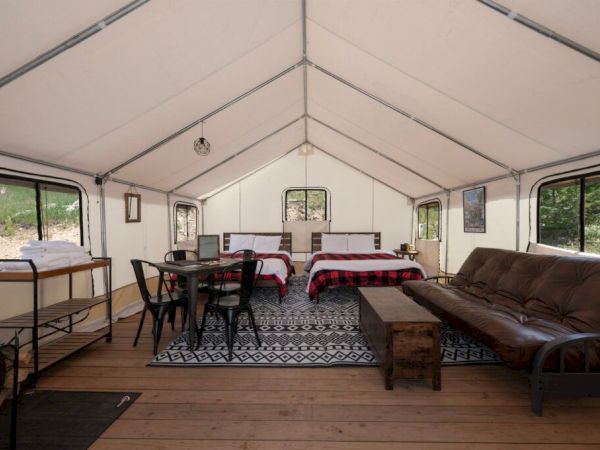 A spacious tented living area with a long table, comfortable seating, a sofa, a coffee table, and a cozy rug, set up for gatherings.