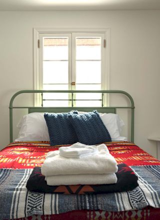 A tidy bedroom with a quilted bed, two pillows, nightstands, and a window letting in natural light, creating a cozy, simple space.