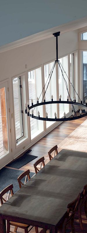 A long modern cafe or bar with large windows, wooden tables, stools, and a chandelier hanging overhead.