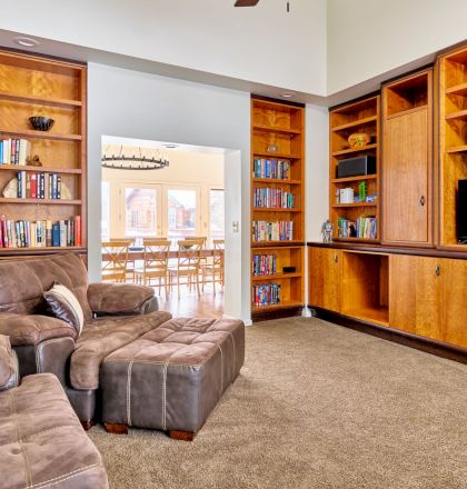 A cozy living room with built-in wooden bookshelves and cabinets, a brown sectional sofa, and a flat-screen TV in the wall unit.