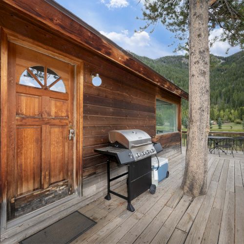 A wooden cabin with a German Shepherd beside a glass door, sunny outdoors, and trees in the background. Top it at 140 characters, always ending the sentence.