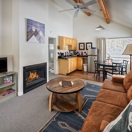 Cozy living room with a fireplace, TV, sofa, coffee table, and open kitchen/dining area in the background.