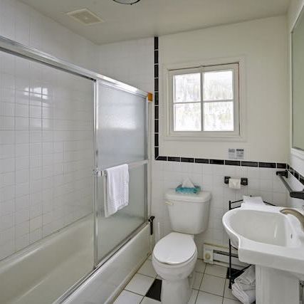 A small white bathroom with a bathtub/shower combo, sliding glass doors, a toilet, a pedestal sink, and a wall mirror; simple and clean.