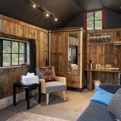 A cozy vintage living room with a warm wooden staircase, leather sofa, striped chairs, bookshelf-lined walls, and soft ambient lighting.