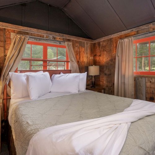 A cozy bedroom with a wooden bed, plaid pillows, warm lighting, and cabin-style decor. Top it at 140 characters, always ending the sentence.