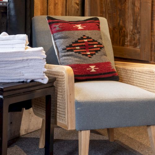 A cozy living room scene with a wooden chair, a plaid throw, a cushion, and a bellows-style fireplace tool set in the background.