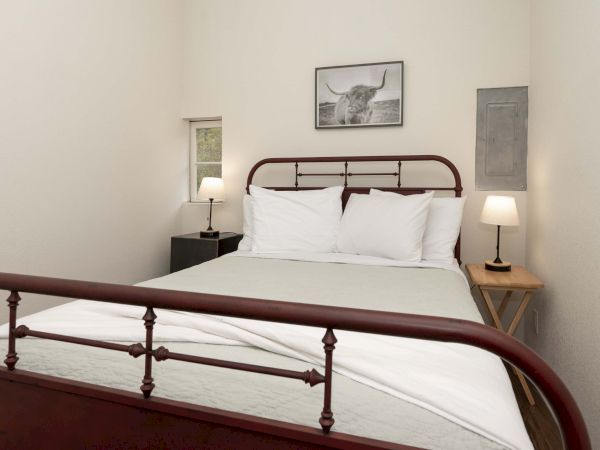 A cozy bedroom with a vintage metal bed, white bedding, two bedside lamps, and simple wall art above the headboard.