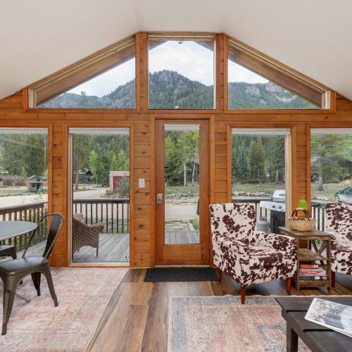 A bright dining area with a long wooden table, white chairs, large windows, and a vaulted ceiling bringing in natural light.