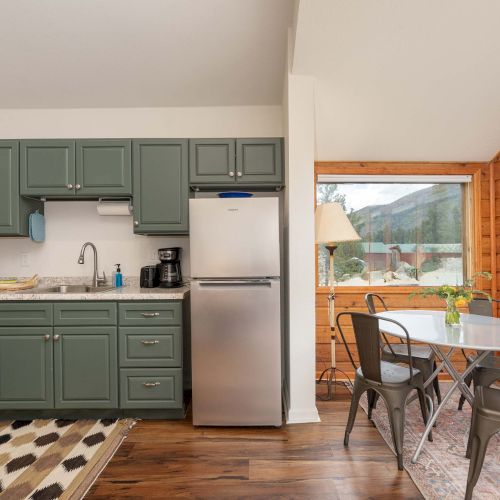 A modern studio with a wooden kitchen island, bar stools, a compact dining area, and a cozy living space with a sofa and wall shelf.