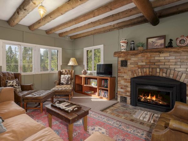 Cozy living room with a brick fireplace, wooden beam ceiling, a sofa set, coffee table, and a small TV stand by the window, warm and rustic.