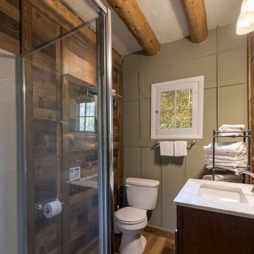 A cozy, sunlit craft-filled room with wooden beams, a loft, plants, books, and warm seating along a brick wall.