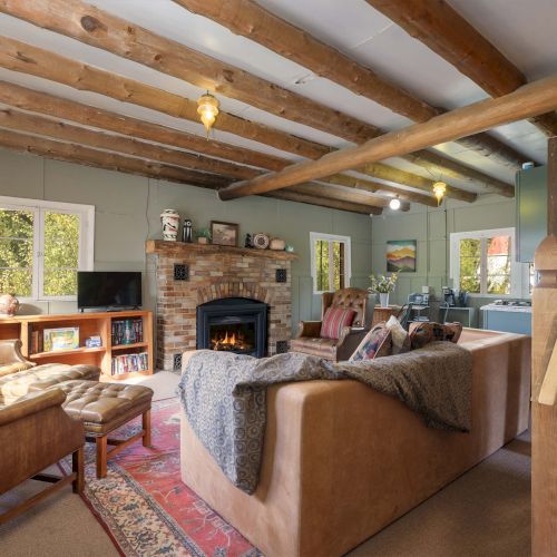 Cozy kitchen and dining area with wooden beams, warm lighting, and a small breakfast bar; open shelves and cozy seating create a rustic showroom.