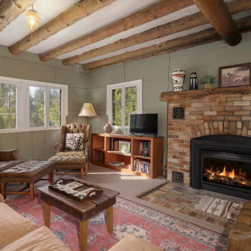 A cozy, rustic living room with a stone fireplace, wooden beams, plush furniture, and warm ambient lighting, inviting relaxation.