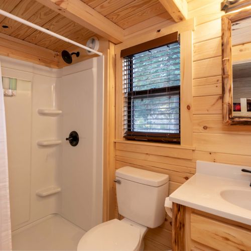 A cozy hotel room with a single bed, warm lighting, a small desk, window with blinds, and a doorway leading to a bathroom or hallway.