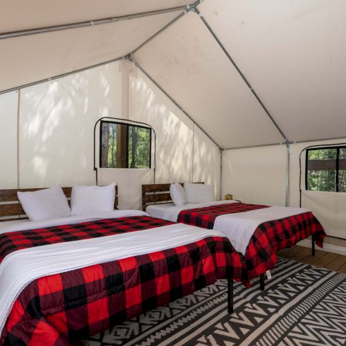 A cozy rustic bedroom with a bed off to the side, a plaid red blanket, warm lamps, and soft natural light streaming through a window.