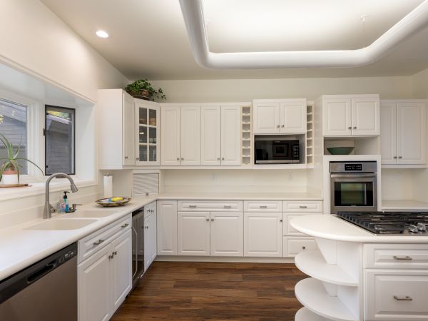 A bright, modern white kitchen with ample cabinetry, stainless appliances, and a curved island, featuring a gas range and built-in microwave.