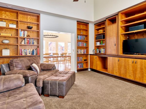 Cozy living room with built-in wooden bookshelves, a brown sectional sofa, and a wall-mounted TV in a warm, organized space.