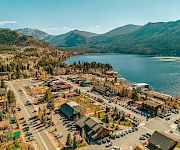 A small lakeside town with a marina, colorful buildings, and a parking lot, nestled among green hills and a calm blue lake.