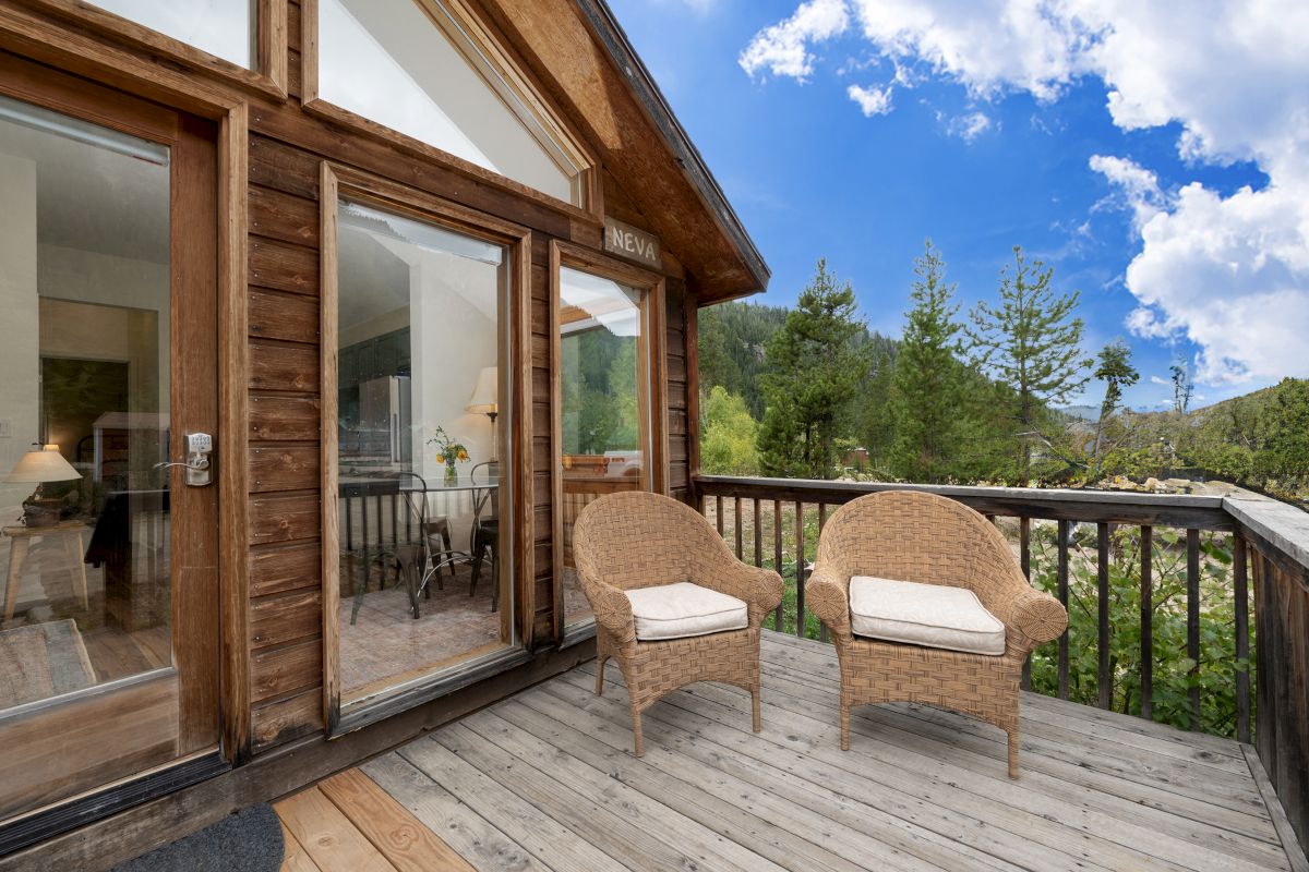A wooden balcony with two wicker chairs and a view of trees and blue sky from a cabin.
