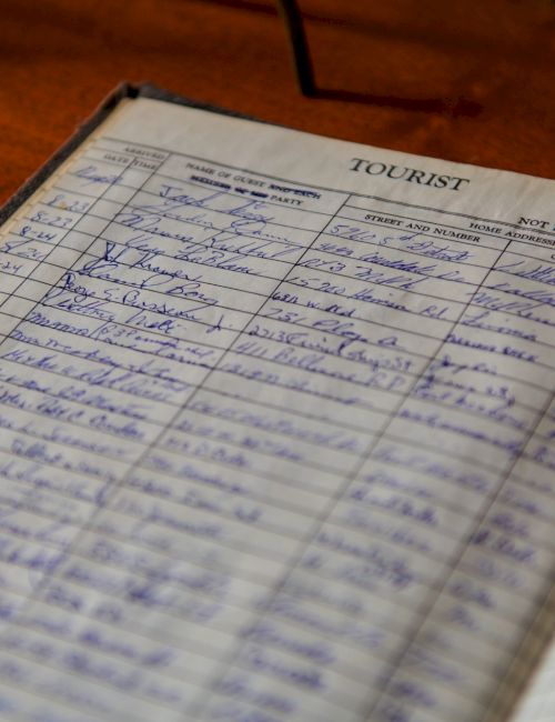 A handwritten guest logbook or traveler&rsquo;s diary opened to pages of names and details, with lines and columns for entries and dates to record visits or stay logs.