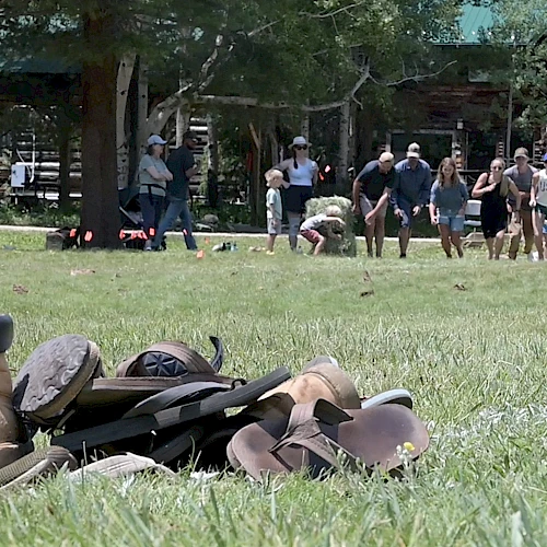 A pile of old hats and boots on grass with people walking and a wooden building in the background.
