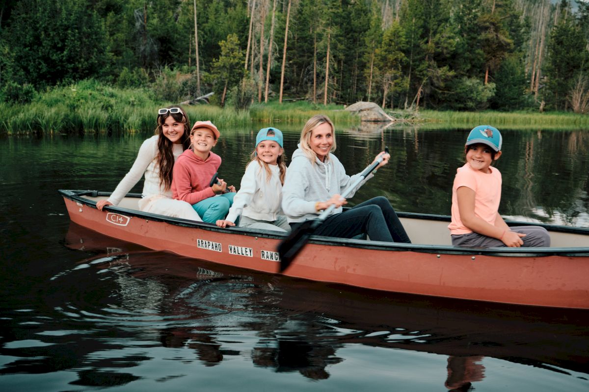 A family rides a red canoe on a calm lake, wheels of a quiet summer adventure as kids smile and look toward the shore.