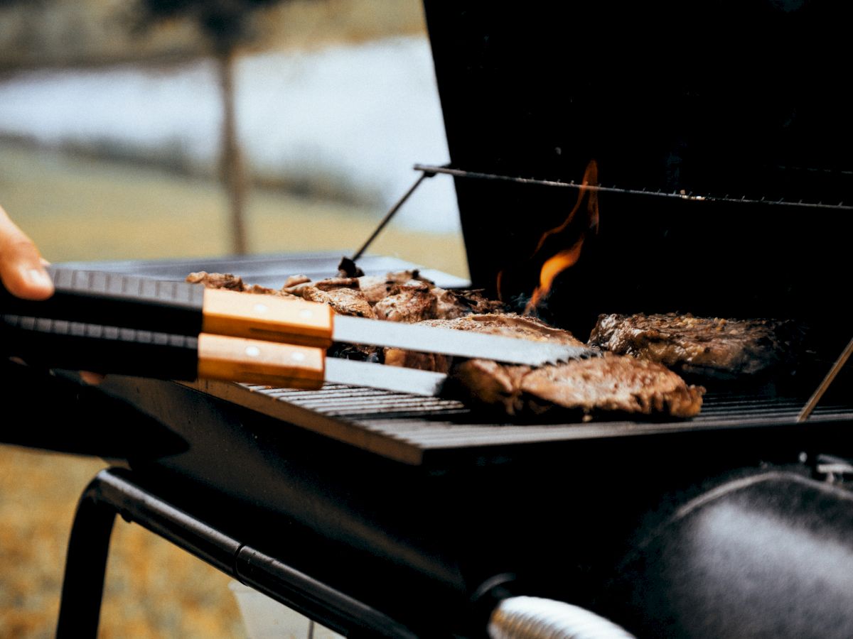 A charcoal grill cooking meat, flames and smoke rising as skewers roast outdoors.