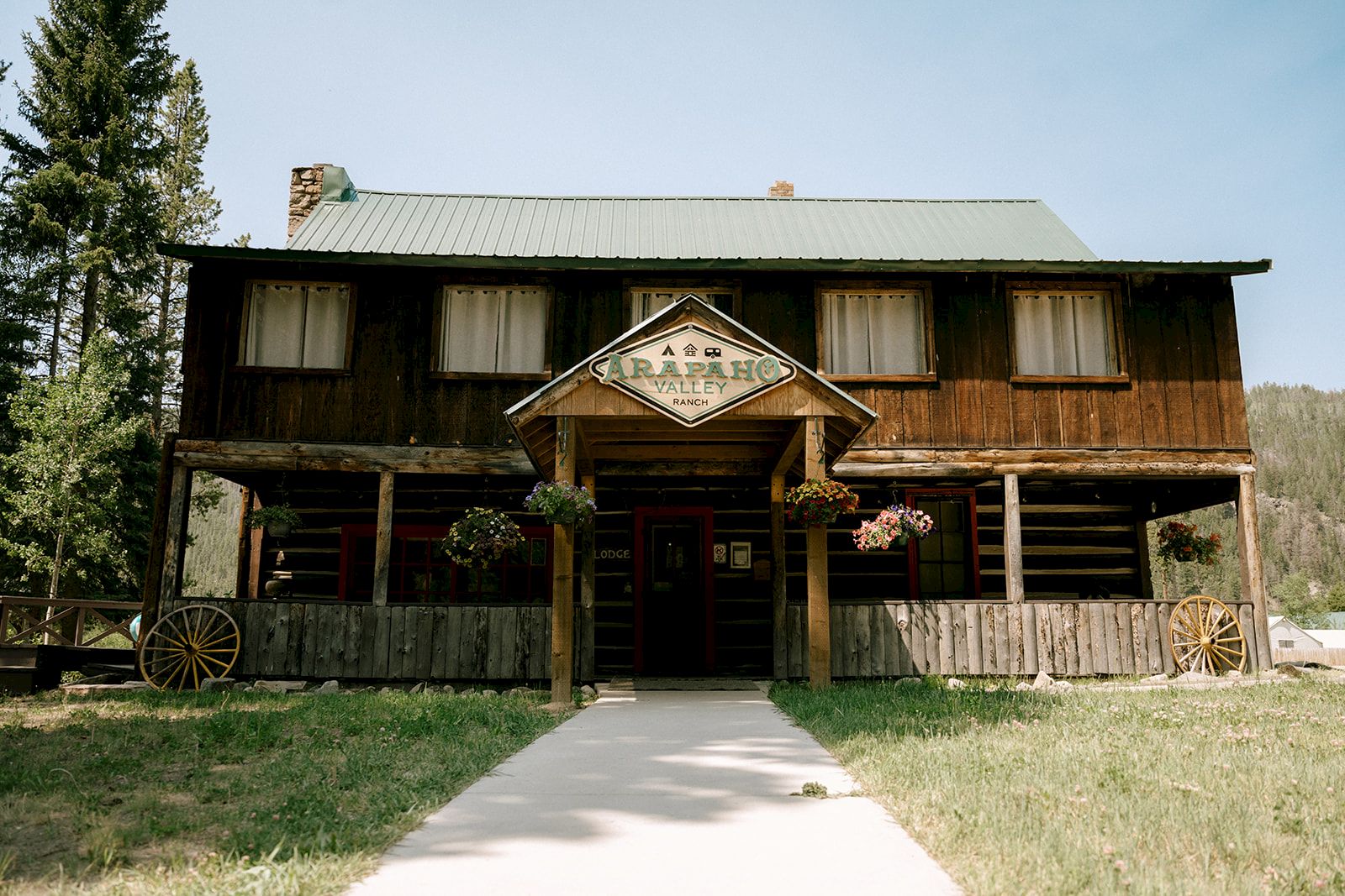 A rustic ranch lodge building with &ldquo;Carapaho Valley Ranch&rdquo; sign, flowers, and a path leading to the entrance.