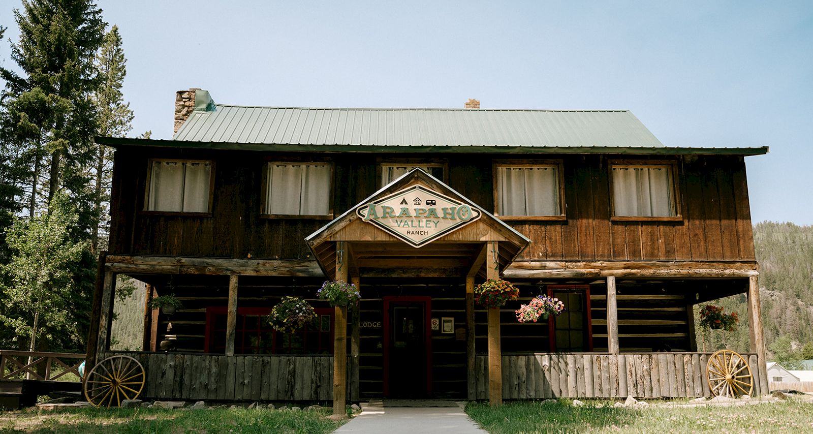 A rustic ranch lodge building with &ldquo;Carapaho Valley Ranch&rdquo; sign, flowers, and a path leading to the entrance.