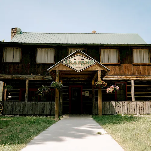 Rustic wooden ranch lodge with a “Caraphaho Valley Ranch” sign, flower boxes, and a path to the entrance.
